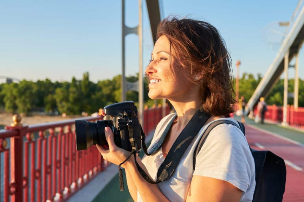 A woman smiling and holding a camera outside. 