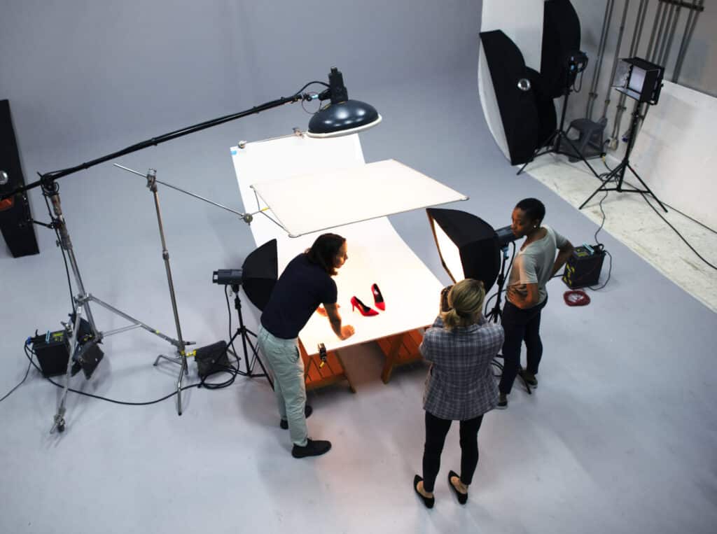 Three students working together on the set of a photography shoot to capture images of shoes.