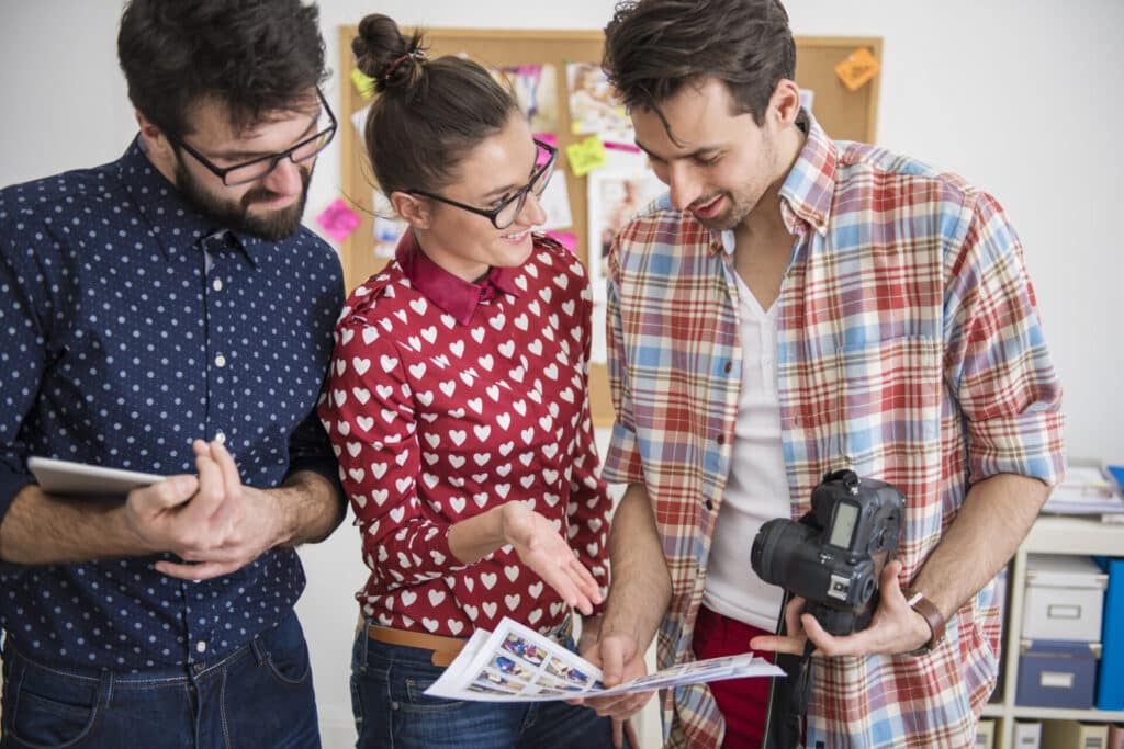 Three students looking at digital prints and holding a camera.