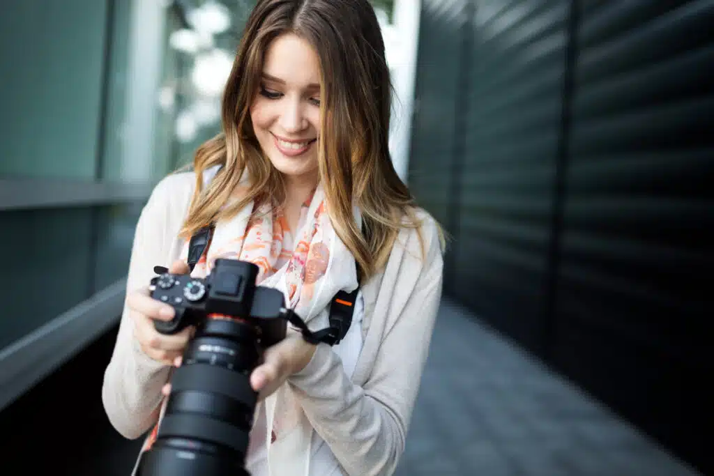 A woman holding a camera and looking at it while smiling.